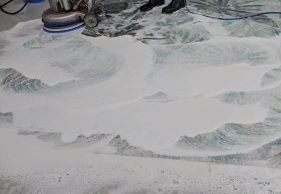 Rotary brush machine scrubbing a patterned rug with foam